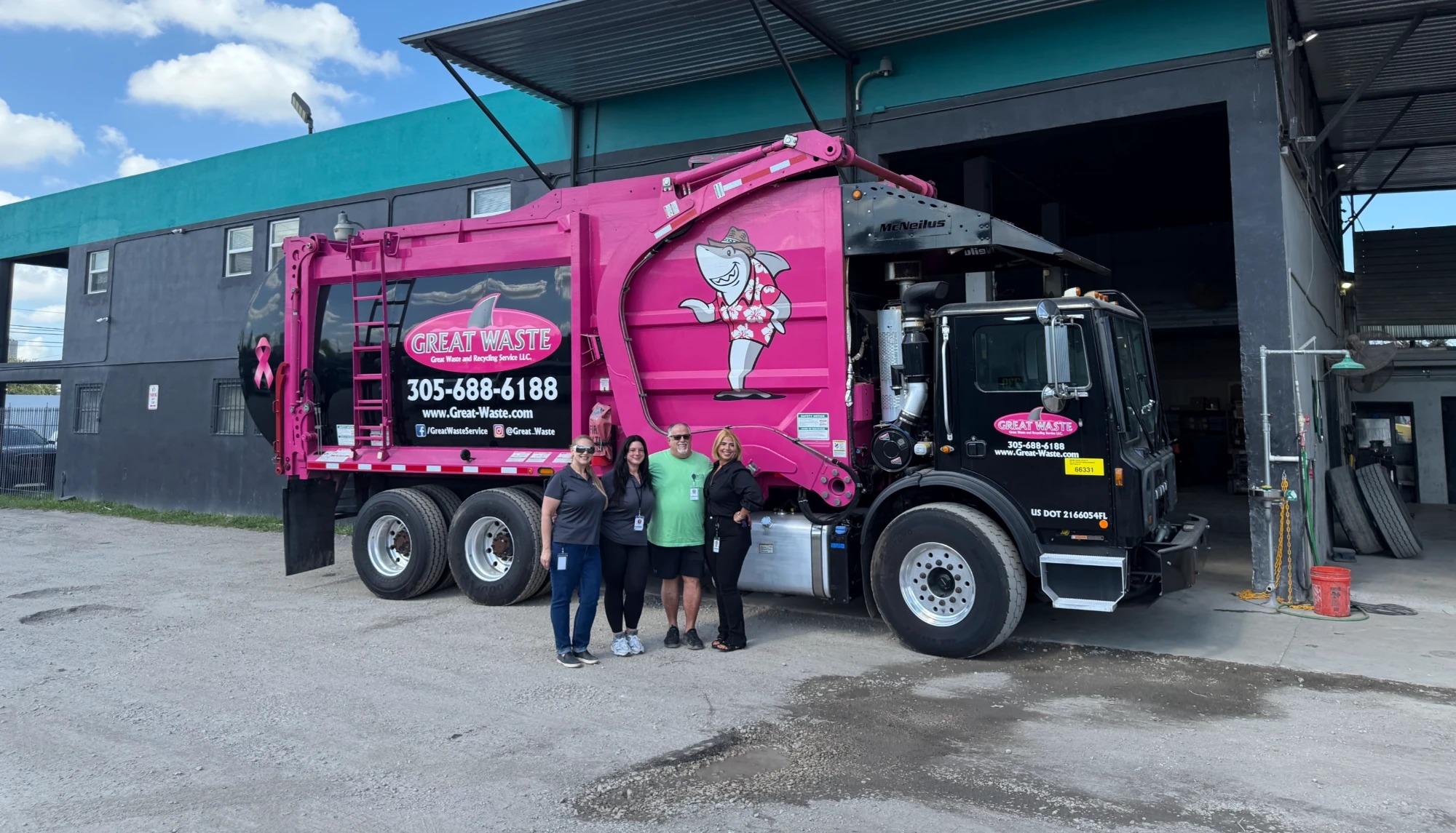 Carlo Piccinonna and his three daughters standing together in front of a pink Great Waste front-loading garbage truck carrying the Paulie the Great White Shark mascot, outside the company service yard